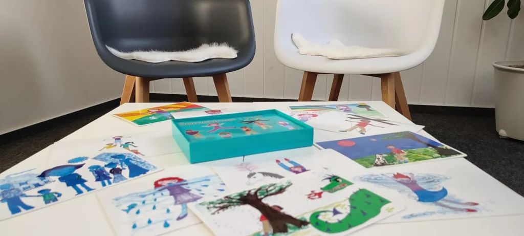 Bunte Bildkarten liegen auf einem Tisch, dahinter zwei Stühle.