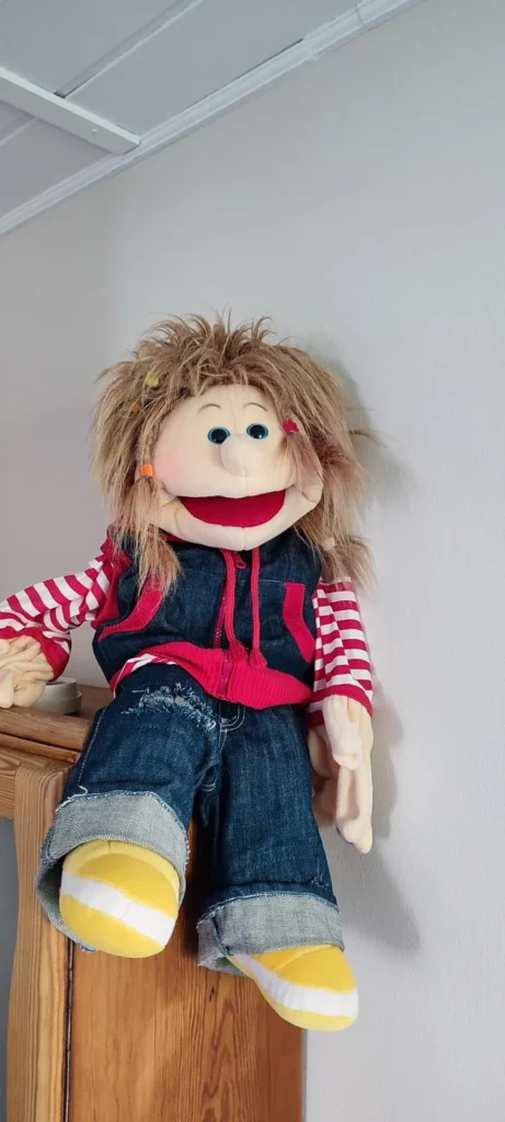 Eine Handpuppe mit Jeans und Ringelpulli sitzt auf einem Schrank.