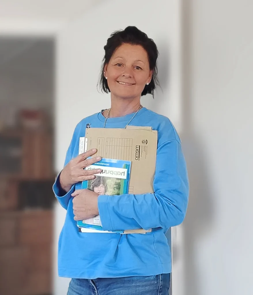 Nathalie Lehmann steht lächelnd in ihrer Praxis und hält Unterlagen im Arm.